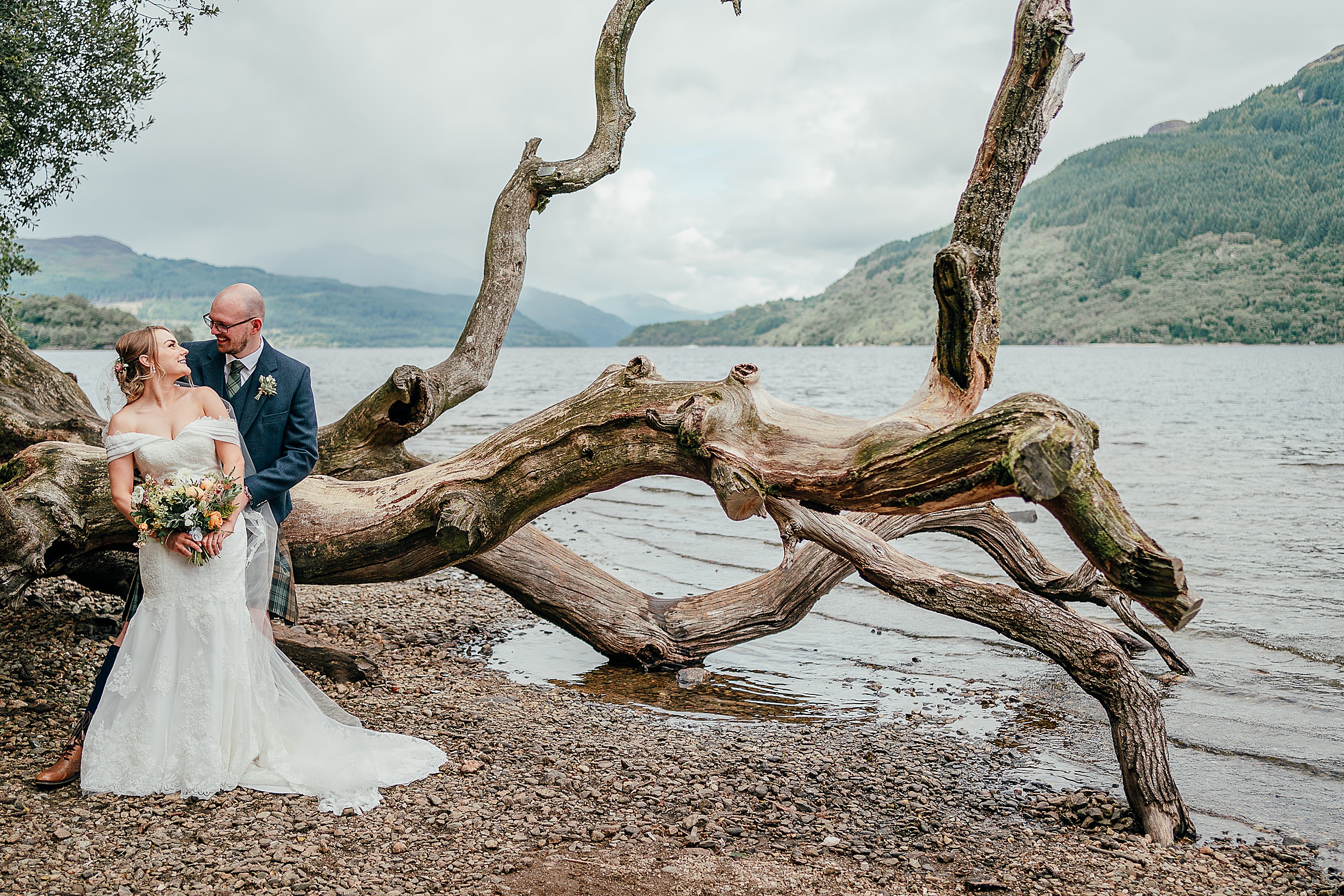 groom holding brides waist from behind looking into each others eyes loch and green hills in background loch lomond micro wedding