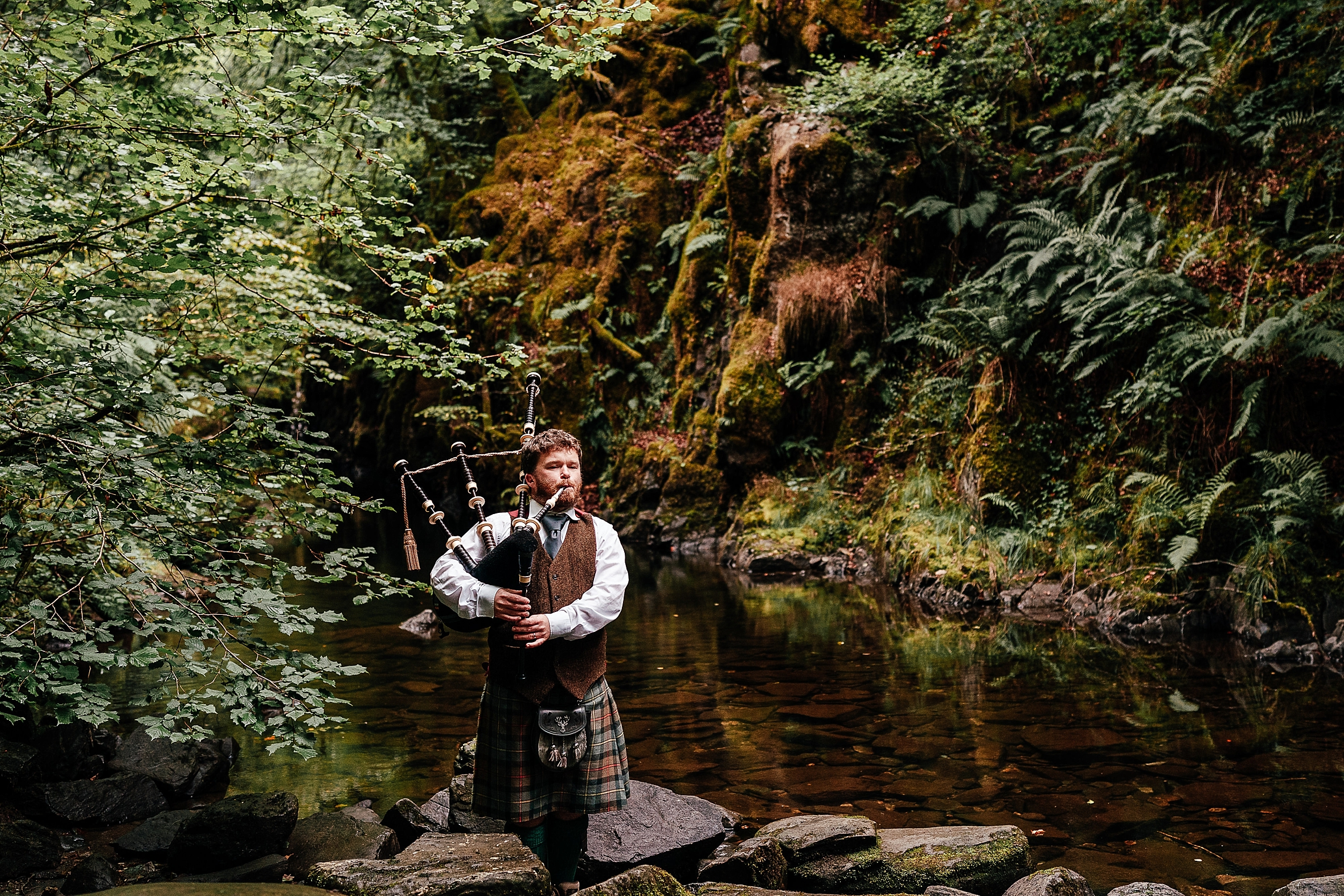 a piper is a wedding traditions scotland playing the bagpipes in a glen