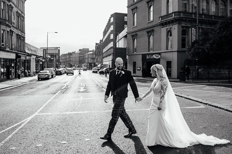 bride and groom walk across a city street in glasgow scotland after their elopement wedding