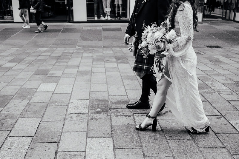 a bride holds a wedding bouquet while walking down buchanan street in glasgow city at her elopement