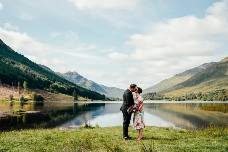 couple kiss infront of hills and loch after they elope to scotland